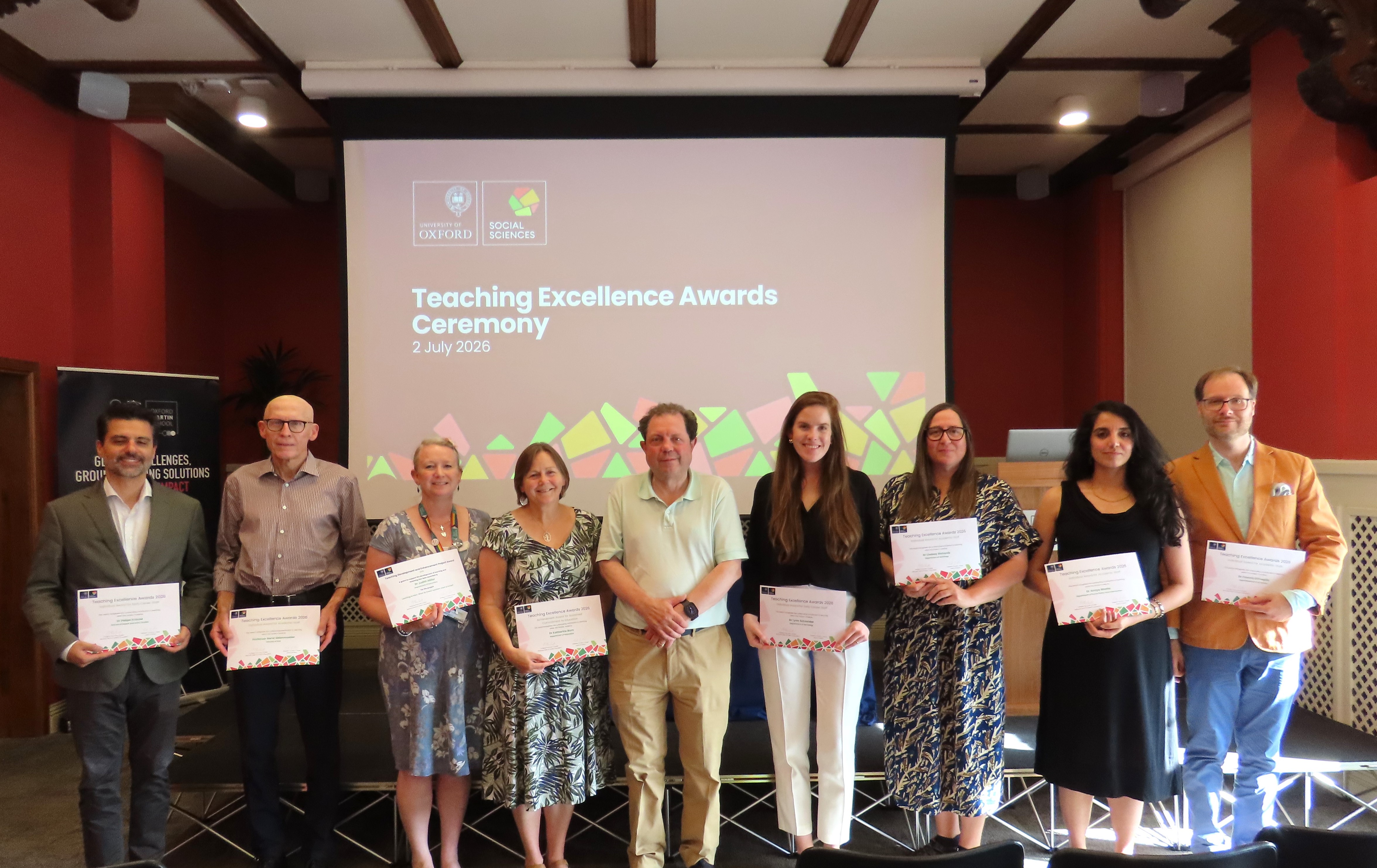 A group of 9 academics standing in a line, holding certificates