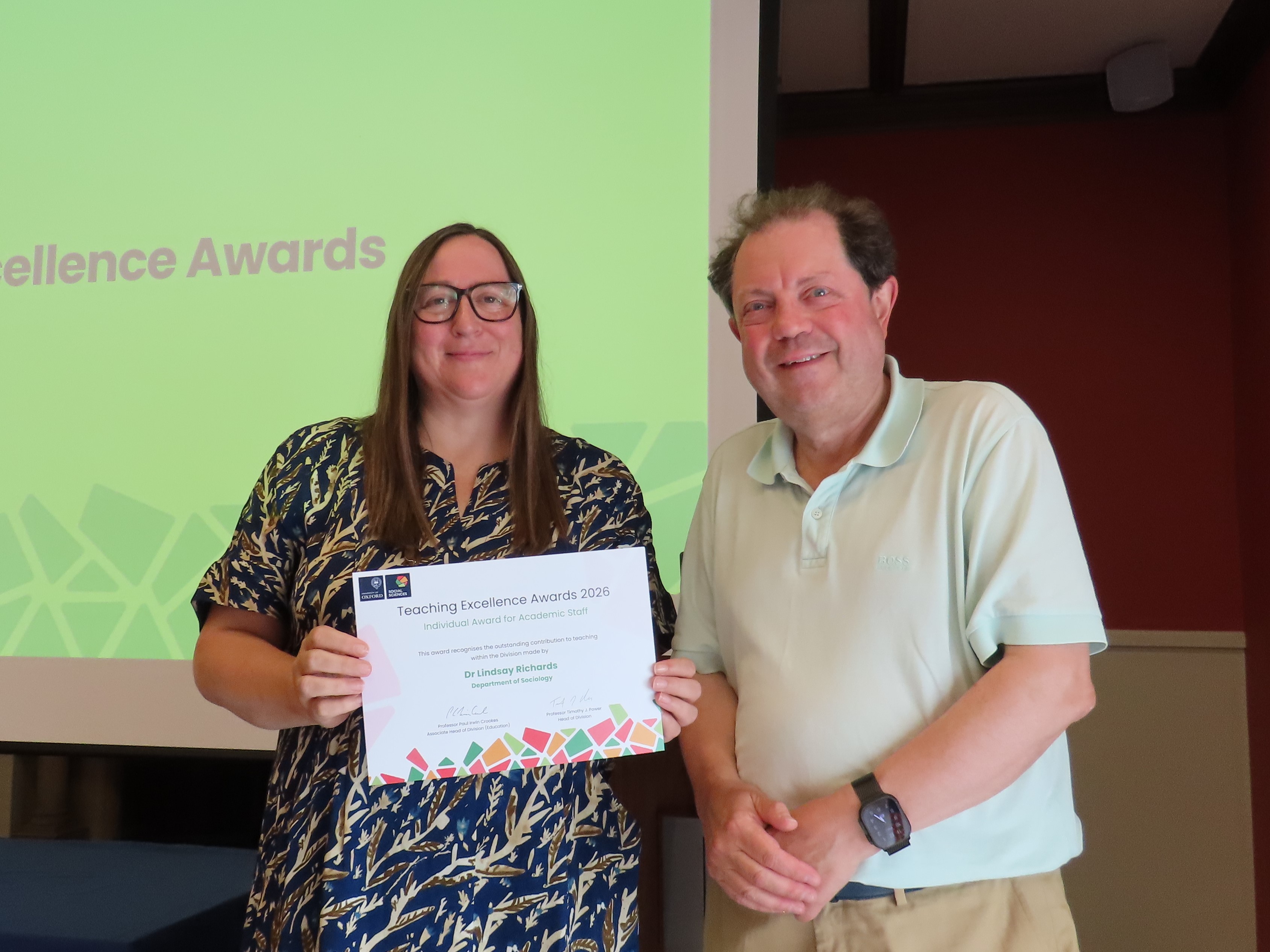 Dr Lindsay Richards, wearing a patterned navy and white dress, holding a certificate next to Professor Paul Irwin Crookes
