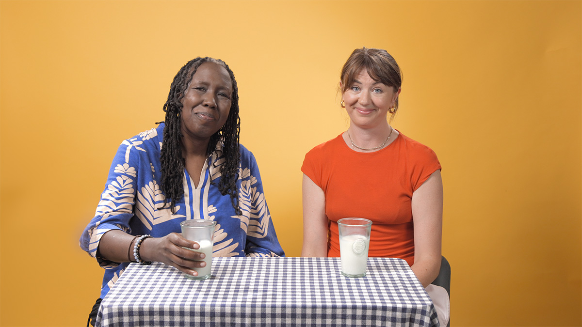 Two women sit at a table, each has a glass of milk in front of them
