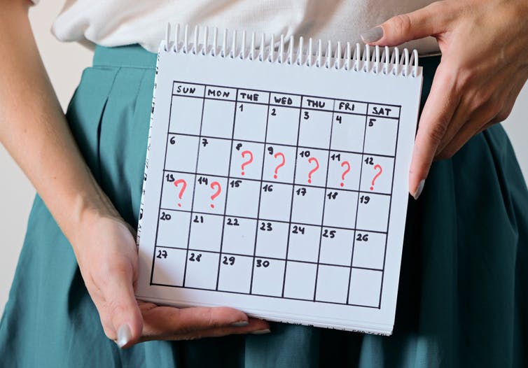 The hands of a woman holding a calendar, which shows 7 consecutive days marked with a question makr