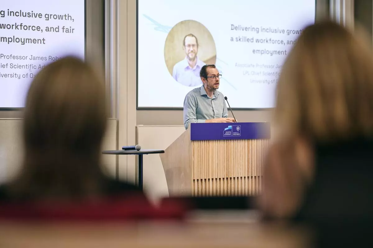 White man wearing glasses and a shirt addresses the audience from a lectern