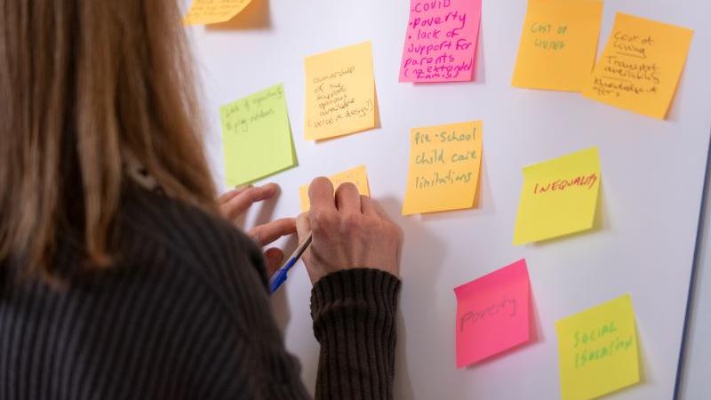 A delegate adds her thoughts to a board covered in post-it notes about the challenges facing early years provision