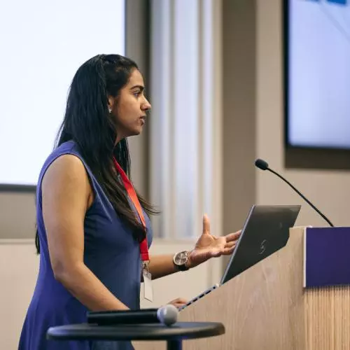 A woman with long dark hair addresses the audience from a lectern