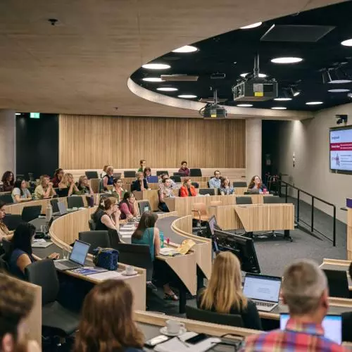 A bird's eye view of a full lecture theatre while two women address the audience from a lectern