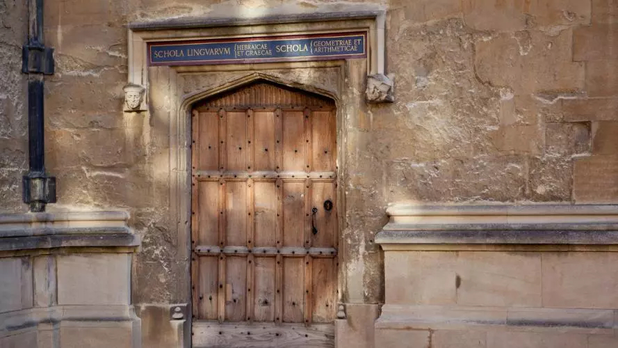 A wooden door in an old stone building, with painted words in Latin script over the frame