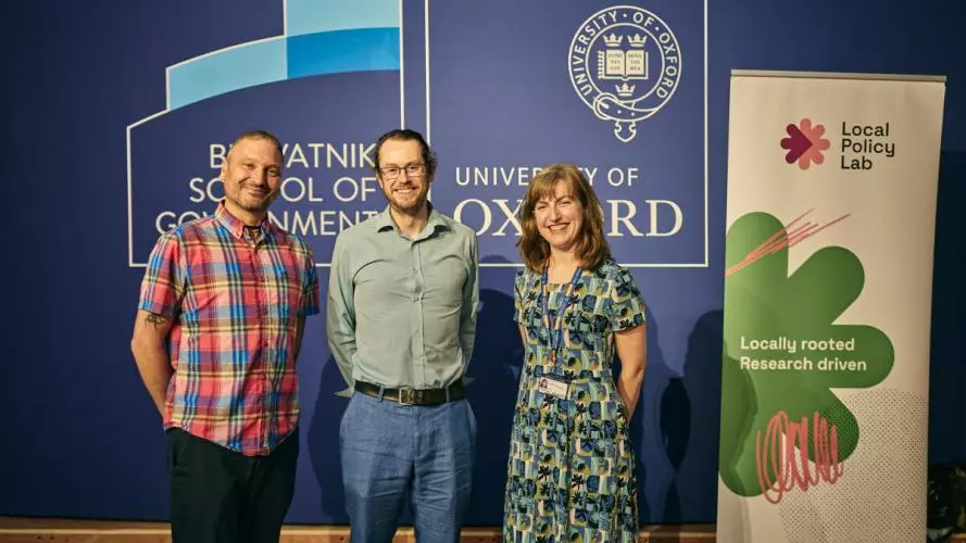 Two men and a woman stand in front of a board smiling at the camera