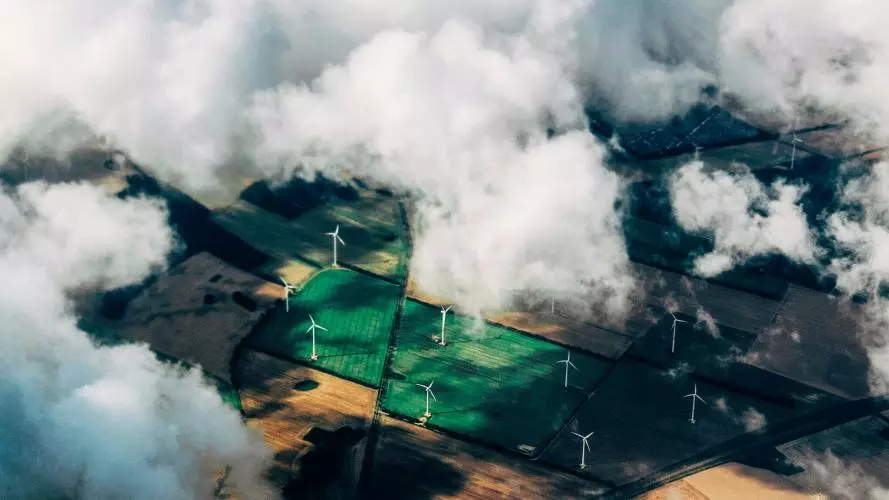 Aerial view of wind turbines in green and yellow field half hidden by white clouds
