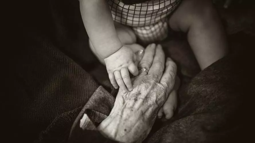 A baby holds an old lady's hand