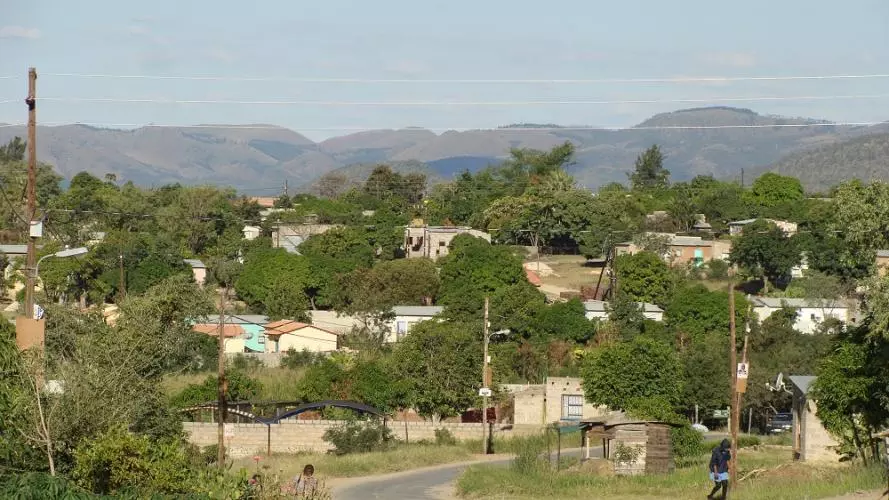 A scene of a rural south african town with overhead power cables and mountains in the background. A road runs through the middle.