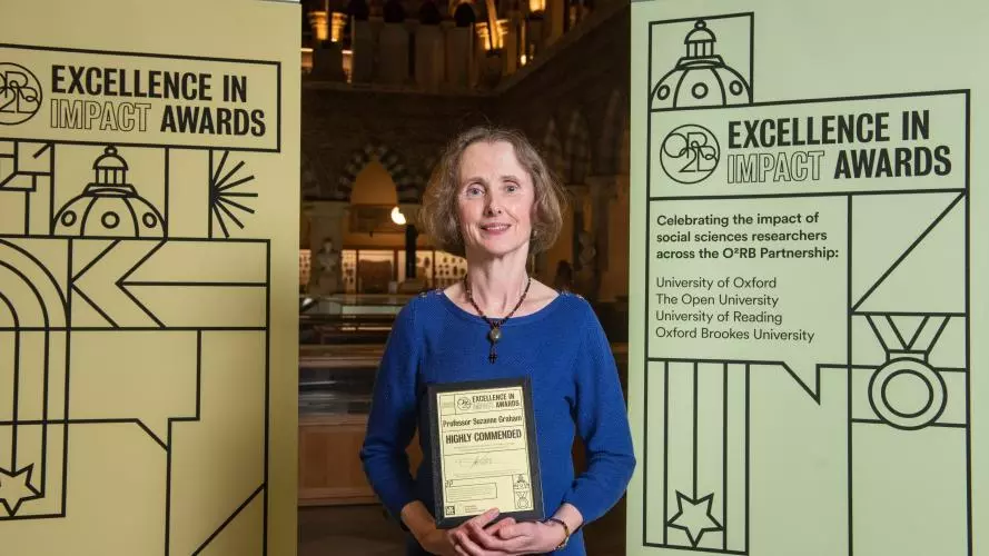 Professor Suzanne Graham holds the Highly Commended impact award, flanked by event branding at the awards reception