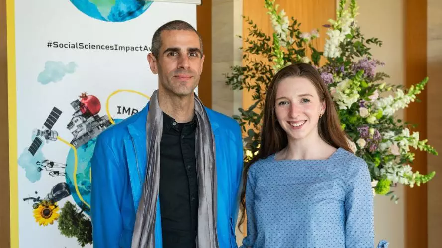 Dr Six Silberman and Aislinn Kelly-Lyth smile to camera.  In the background is the Impact Awards branding and a flower arrangement.