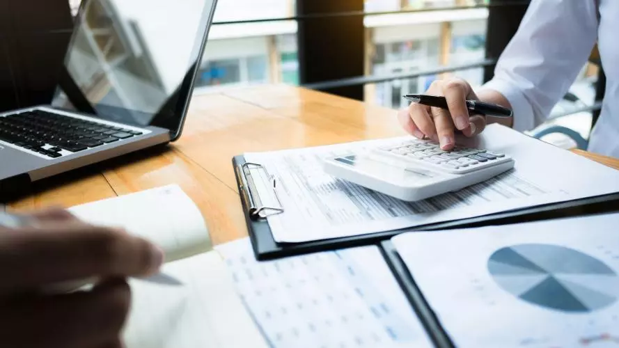 Two businessmen work over a calculator and some papers showing financial data