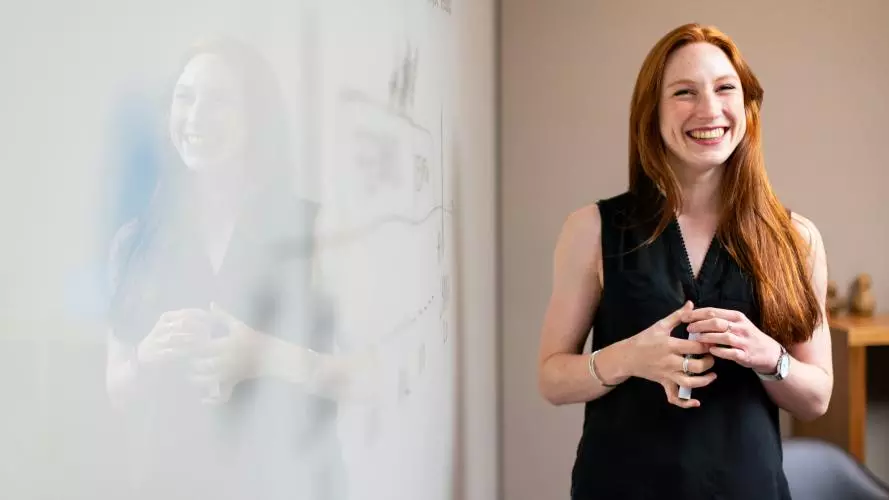 Female academic standing next to a whiteboard smiling and holding a pen 