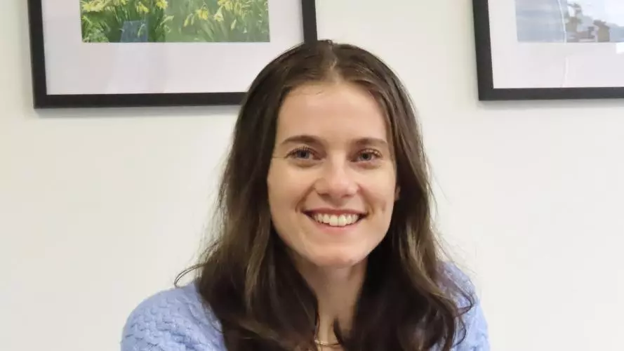 Faith Inch has shoulder length brown hair, wearing glasses smiling at the camera.
