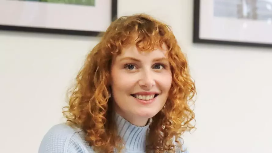 kate oconnor, ha shoulder length red hair, wearing a blue top smiling at the camera.