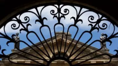 The roof of the Clarendon Building, seen through an arch of ornate railings
