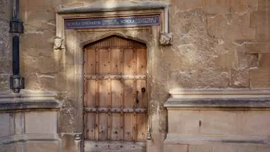A wooden door in an old stone building, with painted words in Latin script over the frame