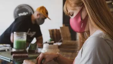 A man and woman, both wearing facemasks, are busy in a workshop