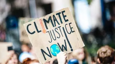 A homemade protest placard reads CLIMATE JUSTICE NOW!