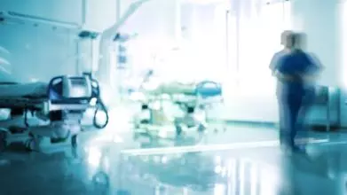 Blurred image of a hospital setting, showing two hospital beds and a medical professional walking past