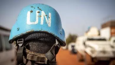 A person wears a blue UN Peacekeeper helmet