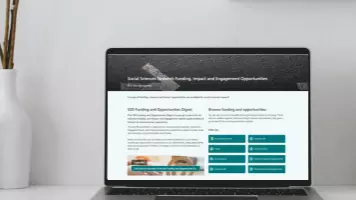 Laptop showing RIE SharePoint on white desk with a white vase and wooden pencil pot
