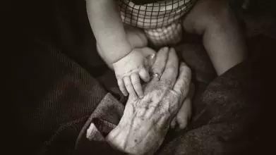 A baby holds an old lady's hand