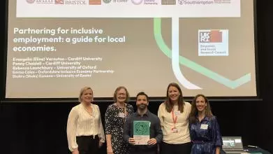 Five people stand in front of a presentation slide titled "Partnering for inclusive employment: a guide for local economies.