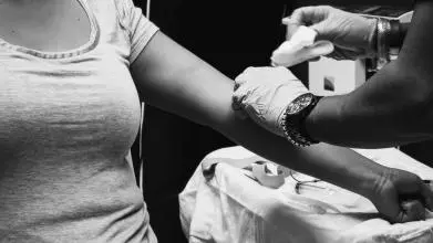 A black and white image of a medical professional, who is wearing gloves, preparing a patient's arm for an injection