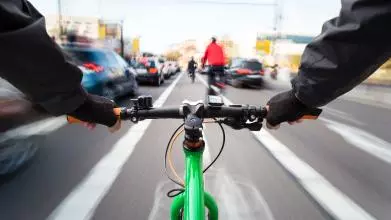 View from the handlebars of a cyclist in the middle of a busy road. Cars and others cyclists around them are blurred.