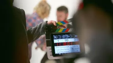 A film crew holds a clapperboard in front of actors on set