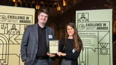 Professor Sandra Wachter and Dr Brent Mittelstadt hold their Highly Commended impact award, flanked by event branding at the awards reception
