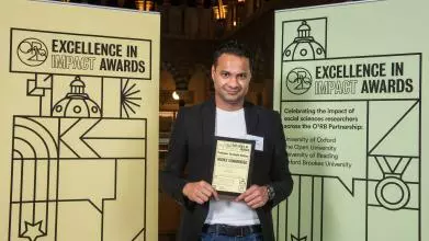 Professor Tarunabh Khaitan holds his Highly Commended impact award, flanked by event branding at the awards reception