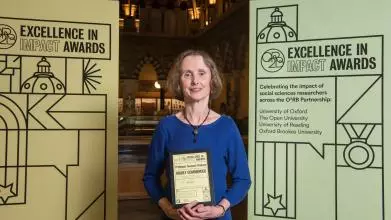 Professor Suzanne Graham holds the Highly Commended impact award, flanked by event branding at the awards reception