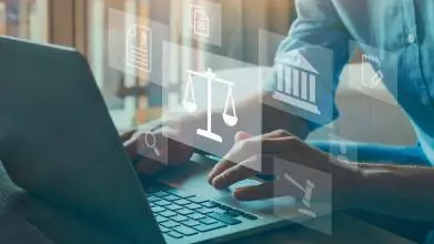 Lawyer types on a laptop surrounded by graphics images of scales of justice, gavel, and data graphics
