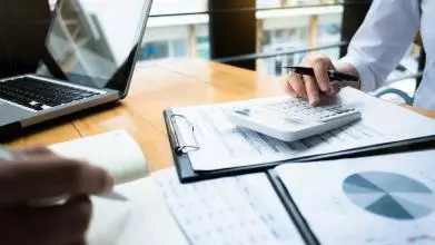 Two businessmen work over a calculator and some papers showing financial data
