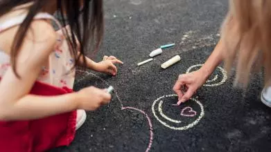 Closeup of little girl and her Mum drawing with colourful chalks on the ground