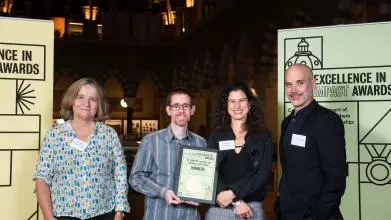 Jamie Lachman, Lucie Cluver, and colleagues smile as they hold their Impact Awards winners certificate, in front of the O2RB Excellence in Impact Awards event branding