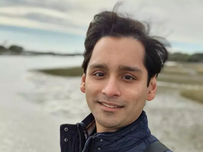 Dr Seenath has short black hair. He is standing outside by a river, wearing a navy quilted jacket.
