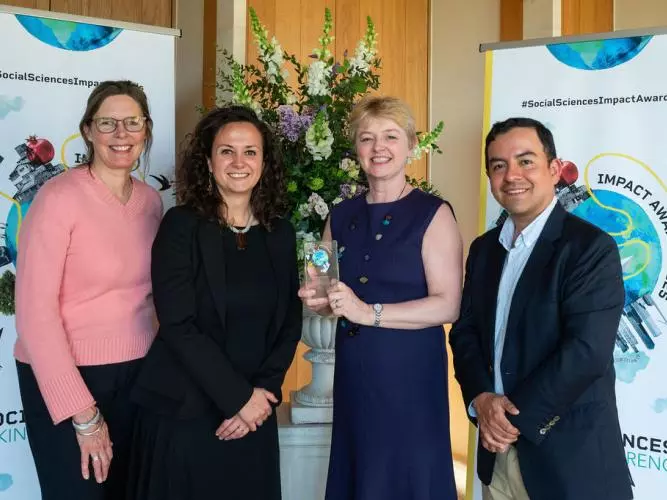 Four Young Lives team members smile and hold the Developing Impact trophy. In the background is the Impact Awards branding and a flower arrangement.