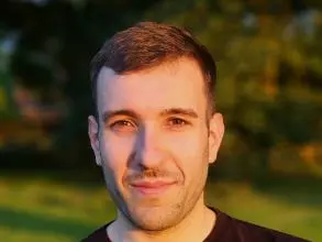 Dr Ippolito has short brown hair and brown eyes. He is wearing a dark jumper, and is standing outside. 