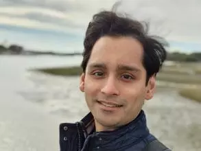 Dr Seenath has short black hair. He is standing outside by a river, wearing a navy quilted jacket.
