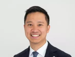 Dr Juin has short black hair. He is wearing a white shirt, blue tie and navy suit jacket. 