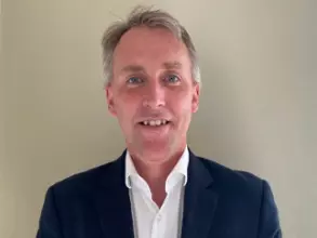 Professor Martin has short grey hair. He is wearing a white shirt and dark blazer. 