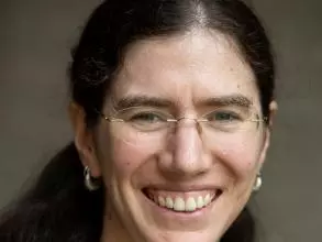 Dr Baldwin has long dark hair, tied in a low ponytail. She is wearing glasses with no frame and smiling widely.