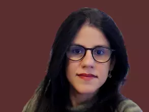 Dr Shahani has long dark hair and large dark-rimmed glasses. She is wearing a grey jumper. 