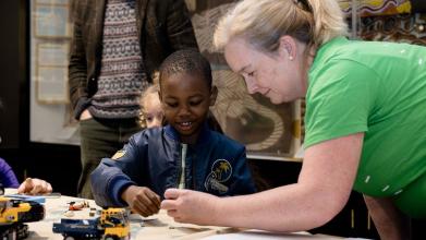A you g boy interacts with a toy digger and an event volunteer