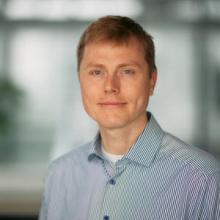 White man with light coloured hair and blue shirt looks at the camera