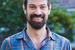 Dr Jones has a dark beard and dark hair, is wearing a baseball cap and a blue plaid shirt 