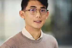 Dr En Hua Hua with short dark hair wearing glasses, a light shirt, and a beige sweater, posing indoors.
